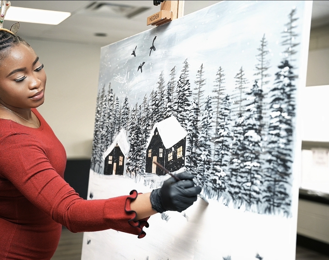 Tosin painting snowy cabins and evergreen trees on a large canvas